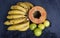 Top view of a fresh sliced orange papaya with seeds inside, a freckled bananas cluster and three green lemons over a blue navy and