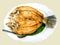 Top view of fried snapper fish topped with fish sauce on banana leaf and white ceramic plate with stainless steel spoon.