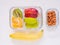 Top view, glass container lunch box of fresh fruit with apple, kiwi, banana, orange and almond on white wooden background. Take aw