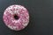 Top view of glazed Donut and pink sprinkles on black board and copy space