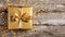 top view of a golden wrapped present with bow on a rustic old table with confetti