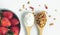 Top view granola and yogurt in wooden spoons on white background with fresh strawberry in white ceramicbowl, idea for banner with