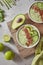 Top view of a green smoothie from avacado, cucumber, kiwi, asparagus with flax seeds and lime slices in a white bowl on