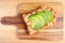 Top view of a grilled cheese toast with tomato and sliced fresh ripe avocado on wooden breadboard