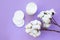 Top view of group of white cotton pads on violet background with cotton branches. Hypoallergenic