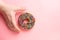 Top view of hand grabbing chocolate frosted donut with sprinkles on pink background. Playful and joyful tasty sugary comfort food