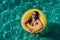 Top view of happy young woman floating in a pool in a yellow donuts. summer and fun lifestyle