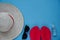 Top view hat with red ribbon, glasses, sanitizer and red flip flop sandals on blue background. Vacation during coronavirus. Summer