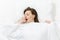 Top view of head of happy brunette young woman lying in bed with white sheet, pillow, blanket. Yawning pretty female