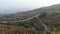 Top view of highway in autumn forest on hill. Shot. Panorama of town on coast near wooded hill. Coastal highway with