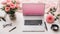 Top view home office desktop with laptop, pink flowers in a vase, notebook,