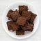 Top view, homemade chocolate brownies on a white plate on a white wooden table. Flat lay, overhead, from above. Close-up