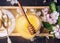 Top view of honey jar with wooden dipper, spoon and spring blossom on honeycomb