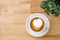 Top view of hot coffee latte with heart shaped milk foam on light wood table background with tabletop small pot of Fittonia nerve