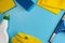 Top view of house cleaning supplies: rubber glove, sponge, cloths, squeegee and detergent on blue background. Copy space