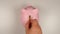 TOP VIEW: Human hand throws a coin into pink pig money box