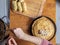 Top view on human hands spreading a metal spoon filling on a stack of baked ruddy pancakes on a wooden background