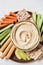 top view of hummus in bowl with arranged cut vegetables slices breadsticks and pita bread