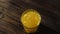 Top view of ice cubes falling in tall glass with fresh orange juice making splashes and bubbles against wooden table