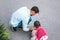 Top view image of little girl and dad drawing with chalks on the sidewalk. Handsome male play together with his cute kid outdoor