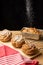 Top view of individual plum cakes with falling sugar, on rustic wooden table with red kitchen cloth, black background,