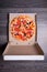 Top view of Italian pizza with ham, tomatoes, and olives in box