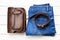 Top view jeans, brown leather bag and a leather belt on a light wooden background. Details of beautiful clothes and accessories. J