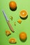 Top view of knife, pieces of oranges and whole one on the bright green surface