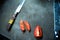 Top view of Knife and pieces of tomato on dark cutting board in kitchen