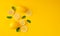 Top view of lemons and green leaves on bright yellow background.