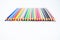 Top view of a line of some different colored pencil crayons arranged on a white background