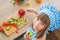 TOP VIEW: Little girl in cook clothes eats a cucumber and looks to the camera