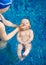 Top view of little kid in diaper swimming on surface of blue water on his back and cropped hands supporting child`s head