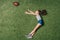 Top view of little sportive girl catching rugby ball on grass,