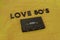 Top View of LOVE 80`S black lettering word with an old black cassette over a yellow cloth