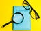 Top view magnifying glass with passport and eye glasses isolated on yellow background.