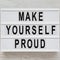 Top view, `Make yourself proud` words on a light box on a white wooden background, overhead view. Flat lay, top view, from above