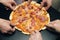 Top view male hands taking slices of pizza with cheese, tomatoes and ham from food delivery. Group of hungry friends