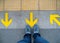 Top view of man feet standing over Arrow symbol on subway platform. Yellow arrow sign on floor at the train station