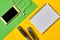 Top view of mobile phone with earphones, white blank notebook and skipping rope on colorful yellow and green background.