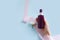 Top view of mock-up of unbranded brown plastic spray bottle, female hand, pink silk ribbon and white flower on a blue background.