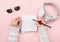 Top view mock up woman`s hands with notebook, headphones, glasses on pink background.