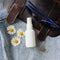 Top view of mockup of unbranded white plastic spray bottle and handbag, sunglasses, camomiles and silver earrings on a denim