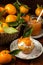 Top view of muffin with cream, tangerine jam and decorative leaf on flower plate with basket of tangerines and jar,