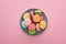Top view of multicolored delicious French macaroons on plate on pink background.