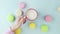 Top view of multicolored French Macarons cookies, a woman's hand removes a cup of coffee from a pastel blue background