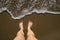 Top view on naked feet on sand in foaming sea wave.