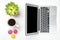 Top view of office desk. Green plant in a pot, cup of coffee, colorful macaroons and modern silver laptop on white background