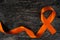 Top view of orange ribbon on dark wood background. Leukemia, kidney cancer, adhd, copd, malnutrition and hunger.