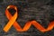 Top view of orange ribbon on dark wood background. Leukemia, kidney cancer, adhd, copd, malnutrition and hunger.